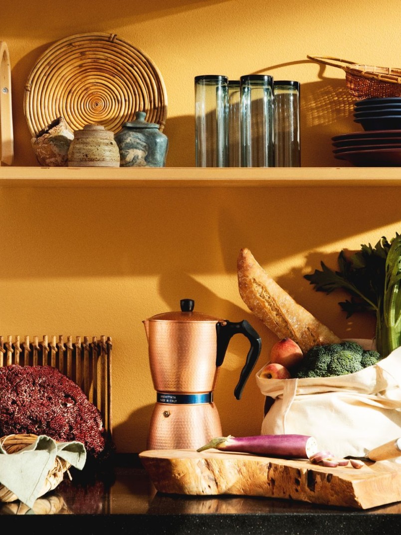 bright warm yellow wall behind busy kitchen desk and shelf