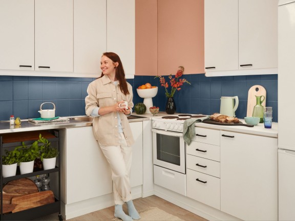 woman in white kitchen with blue backsplash and beige wall